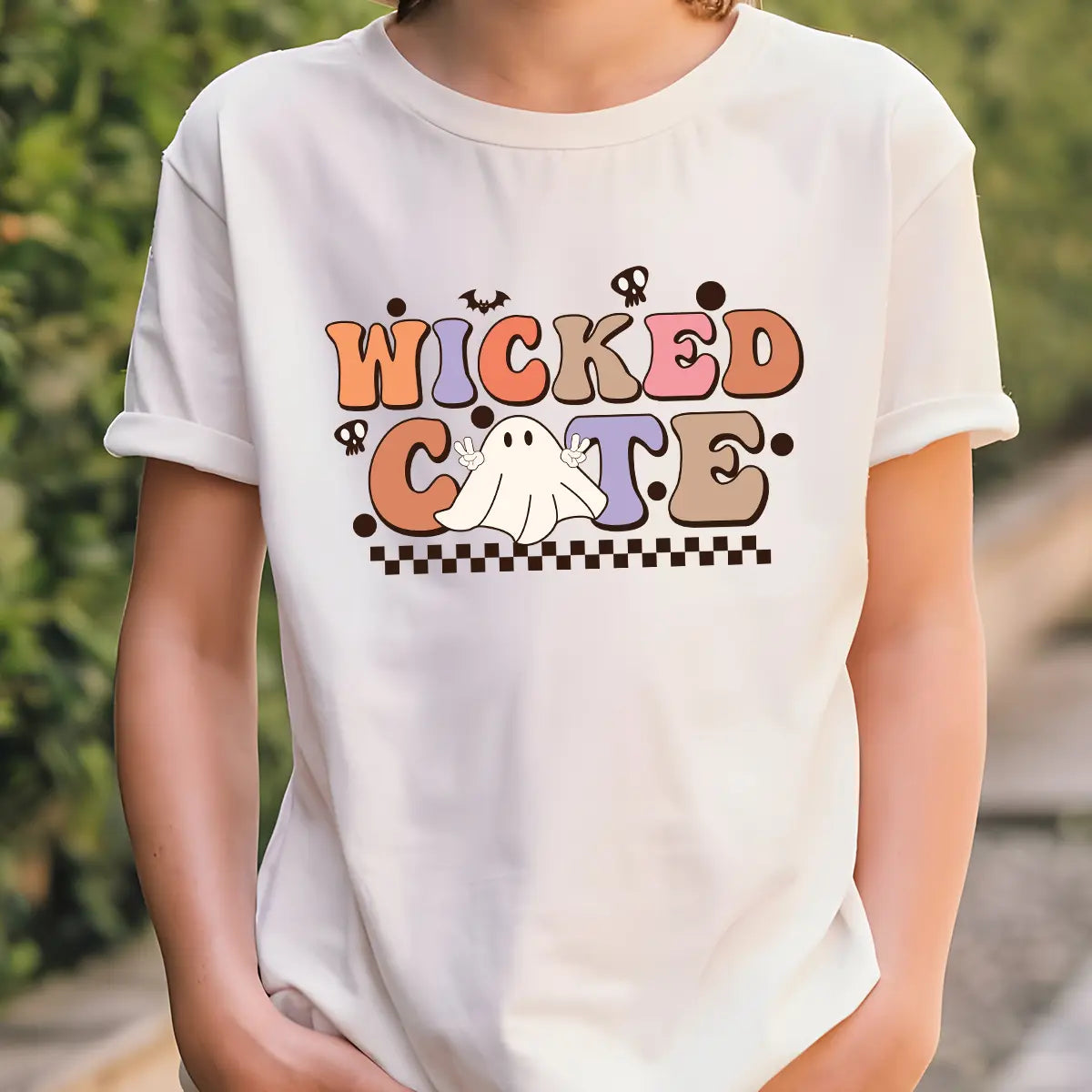 White t-shirt with Halloween design featuring retro bubble letters “Wicked Cute,” peace-sign ghost, checkerboard base, bats, and skulls.