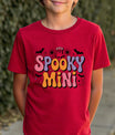 Red t-shirt with Halloween design featuring retro bubble letters “Spooky Mini” in purple and orange, accented by ghost, bats, sparkles, and moons.