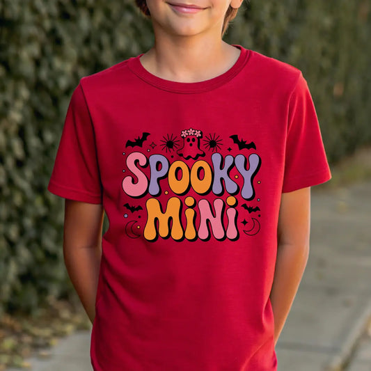 Red t-shirt with Halloween design featuring retro bubble letters “Spooky Mini” in purple and orange, accented by ghost, bats, sparkles, and moons.