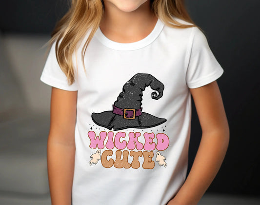 White t-shirt with Halloween design featuring a black witch hat, small ghosts, and text “Wicked Cute” in pink and orange retro lettering, perfect for kids’ spooky apparel.
