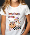 White t-shirt with Halloween design featuring a cute ghost in a pastel witch hat, smiling pumpkin with flowers, retro “Wicked Cute” text, and checkerboard accent.