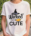 White t-shirt with Halloween design featuring black script “Wicked Cute,” a witch hat above, and a yellow broom graphic across the middle.