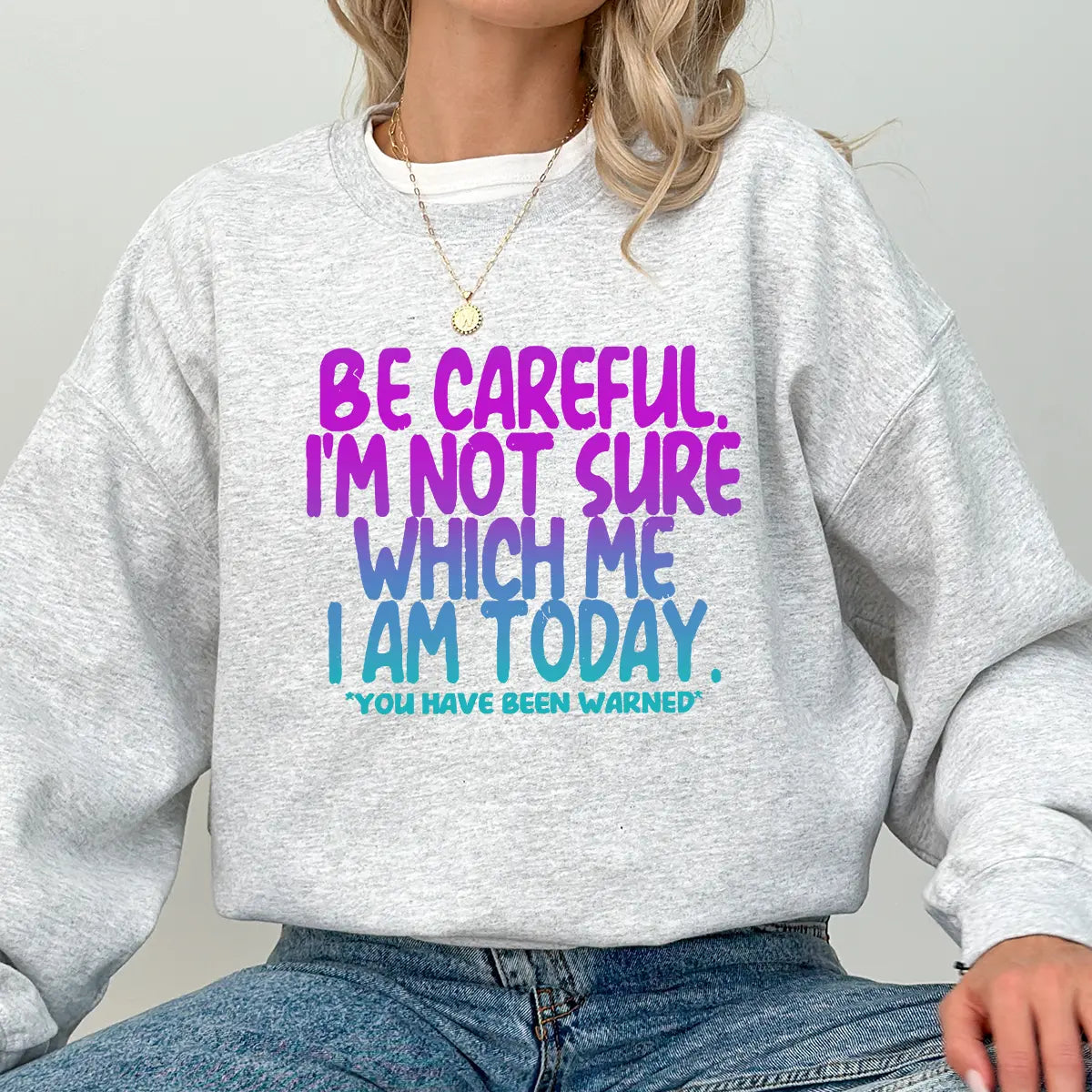 Gray sweatshirt with bold purple-to-blue gradient text reading “Be Careful. I’m Not Sure Which Me I Am Today. You Have Been Warned.” DTF transfer design for funny mood-inspired apparel.