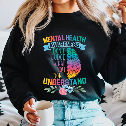 Black sweatshirt with rainbow brain graphic and text “Mental Health Awareness – Don’t Judge What You Don’t Understand” DTF transfer design, accented with flowers, for awareness apparel.