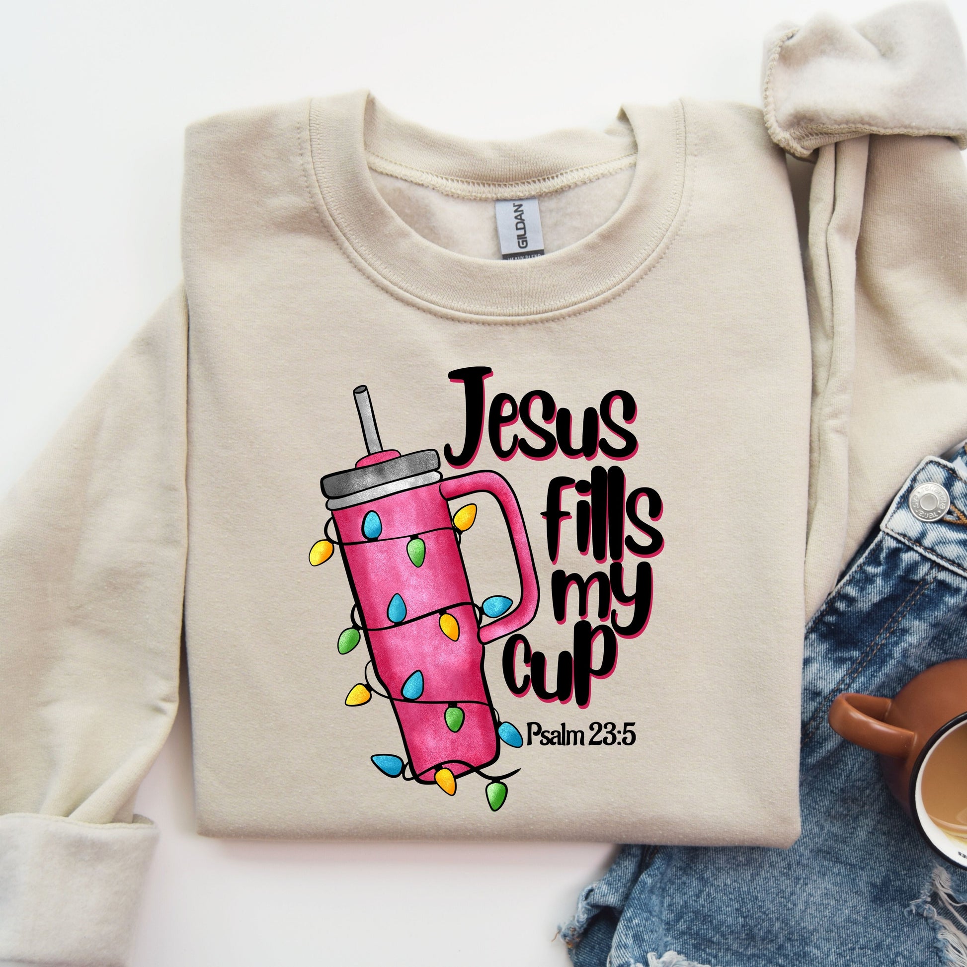 "Jesus Fills My Cup" DTF transfer featuring a colorful tumbler with Christmas lights on a beige sweatshirt.