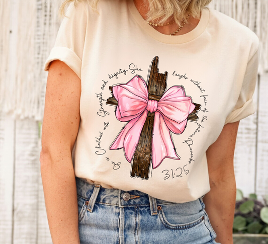 "Strength and Dignity Cross" DTF transfer with a pink bow and scripture text on a cream-colored T-shirt.