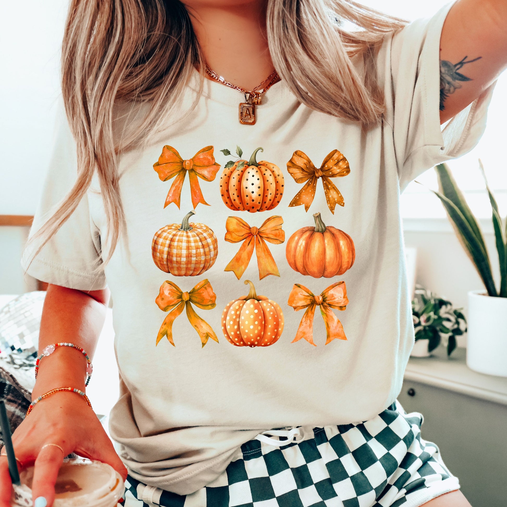 Woman wearing a beige t-shirt with 'Autumn Pumpkins and Bows' DTF transfer featuring various pumpkins and decorative bows