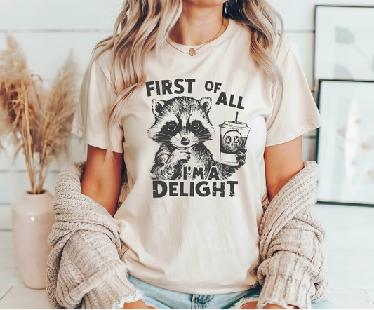 DTF transfer featuring a raccoon with the text 'First of All, I'm a Delight' holding a coffee cup on a beige t-shirt