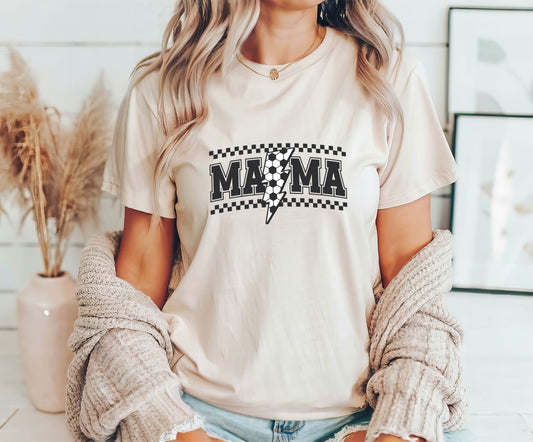 Woman wearing a beige t-shirt featuring "MAMA" with a soccer ball lightning bolt and checkered background, perfect for stylish soccer moms.