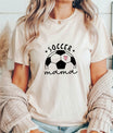 Woman wearing a beige t-shirt featuring a soccer ball with a pink heart and the words 