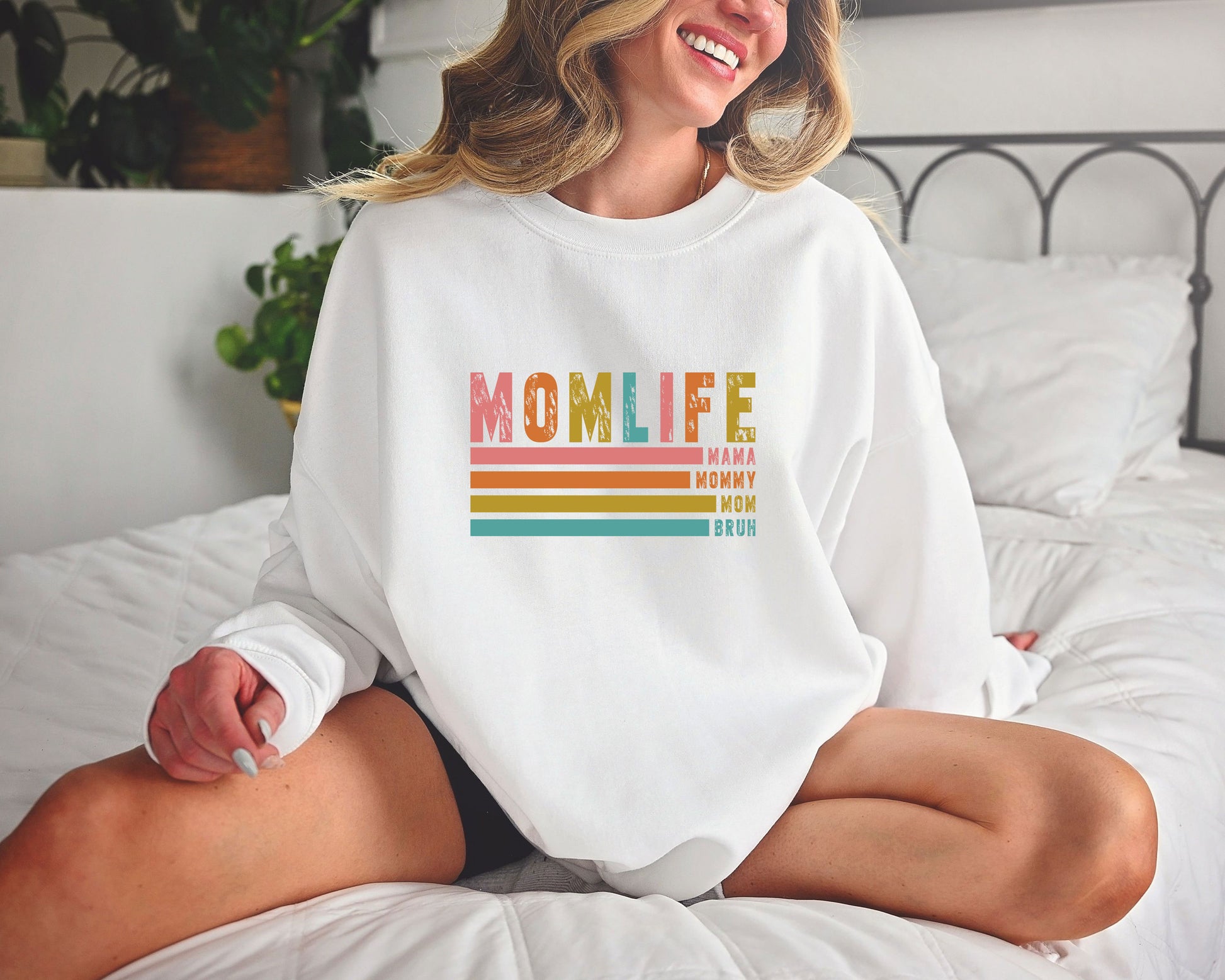 Smiling woman wearing a white sweatshirt with a Retro MOM LIFE DTF Transfer featuring vintage colors and boho-style stripes.