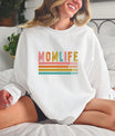 Smiling woman wearing a white sweatshirt with a Retro MOM LIFE DTF Transfer featuring vintage colors and boho-style stripes.