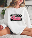 Smiling woman wearing a white sweatshirt with a pink Retro Mama DTF Transfer, featuring a checkered background and vintage-style font.