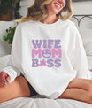 Smiling woman wearing a white sweatshirt featuring a Wife Mom Boss DTF Transfer with a cute, retro-style design in pastel colors.