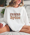 A woman wearing a white sweatshirt with a Mama Spice DTF Transfer, featuring a retro-style font with earthy tones and sparkling accents.