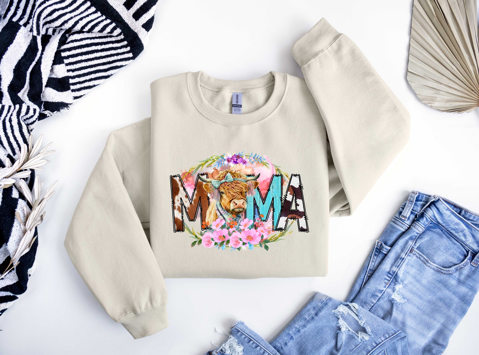 Beige sweatshirt featuring a "MAMA" design with a highland cow illustration and colorful floral accents, perfect for Mother’s Day.