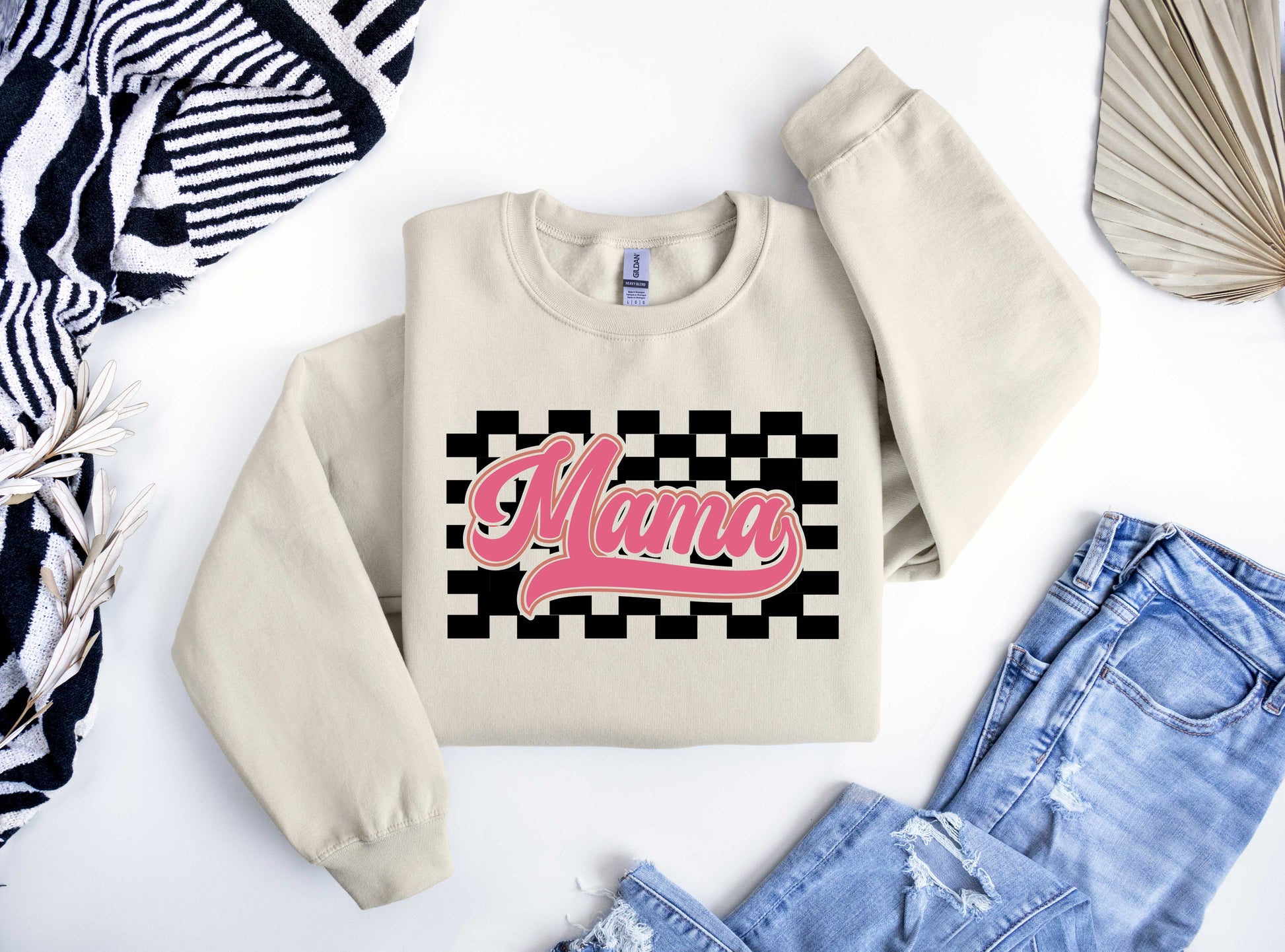 Beige sweatshirt featuring a bold pink "Mama" script over a black-and-white checkered background, perfect for Mother’s Day.