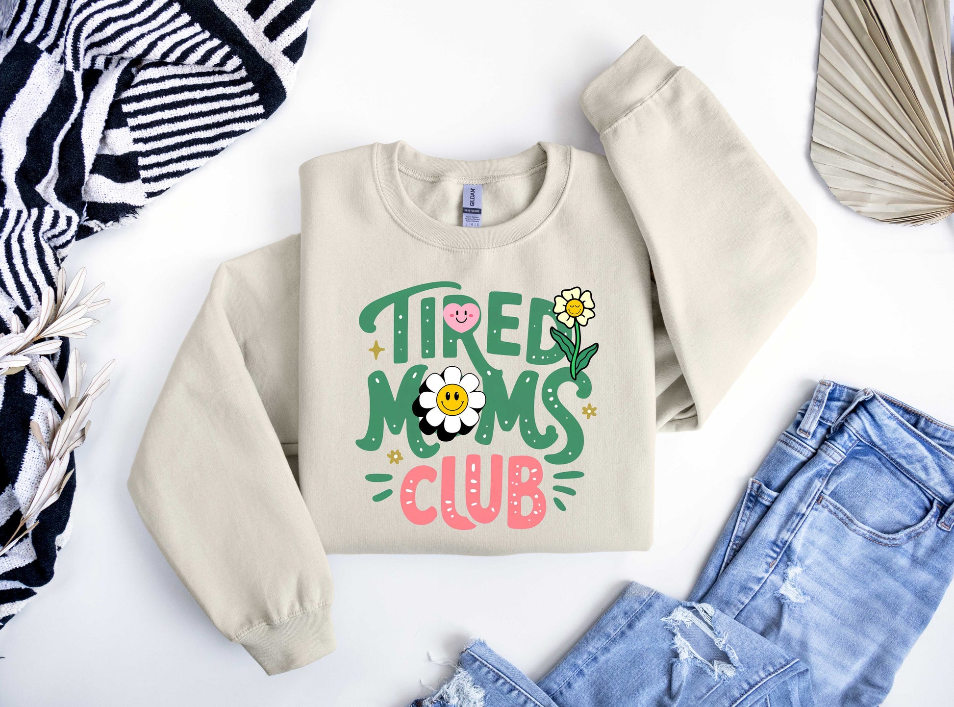 Beige sweatshirt featuring colorful text "Tired Moms Club" with smiley flowers and doodles, perfect for fun Mother’s Day or everyday wear.