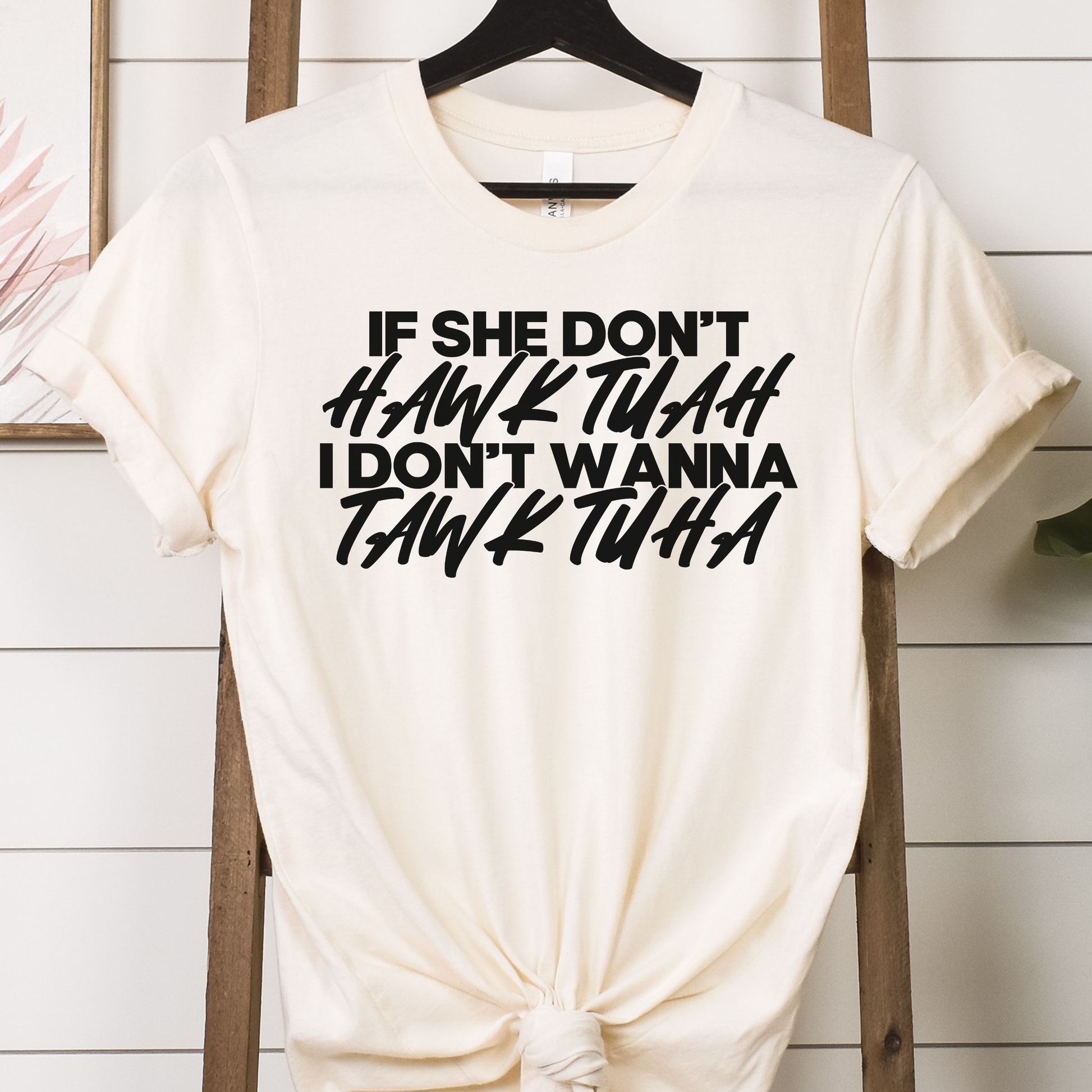 "If She Don't Hawk Tuah" DTF transfer design on a cream t-shirt featuring bold, modern typography in black text.