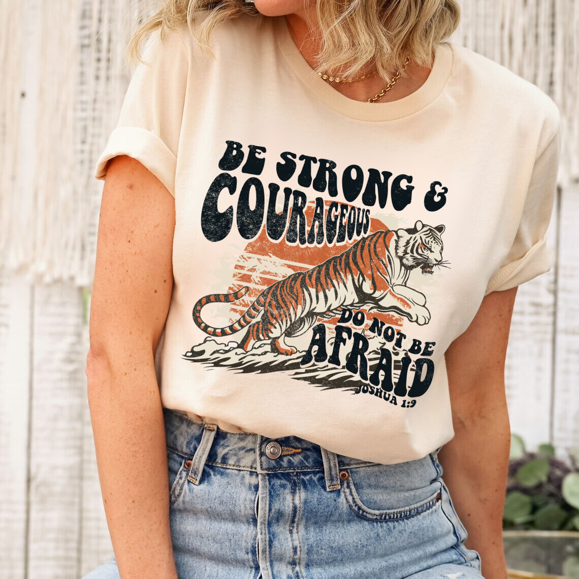 "Be Strong & Courageous" DTF transfer design on a cream t-shirt featuring a tiger illustration and the Bible verse Joshua 1:9 in bold typography.