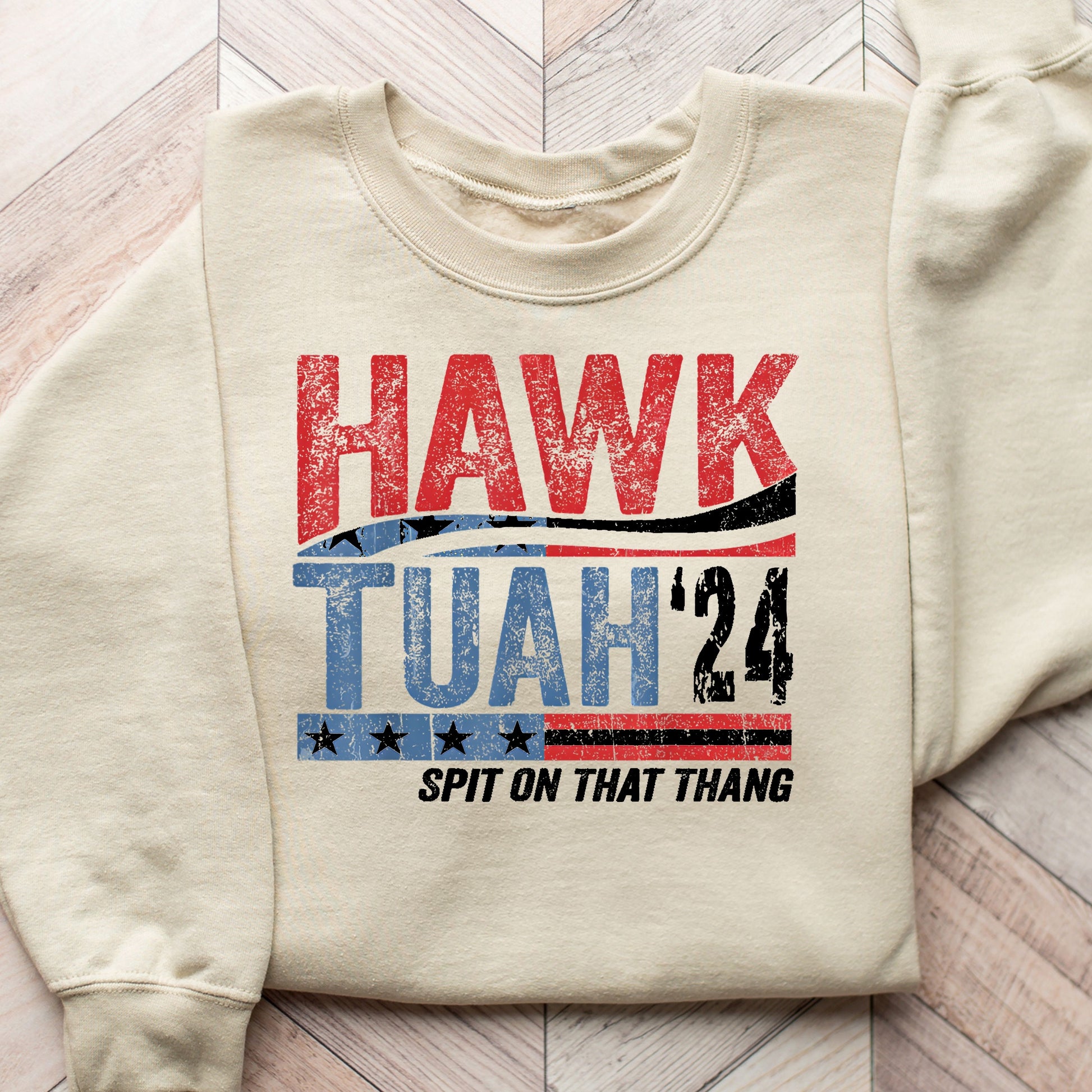 "Hawk Tuah '24" DTF transfer design on a beige sweatshirt featuring distressed red, white, and blue typography with star accents.