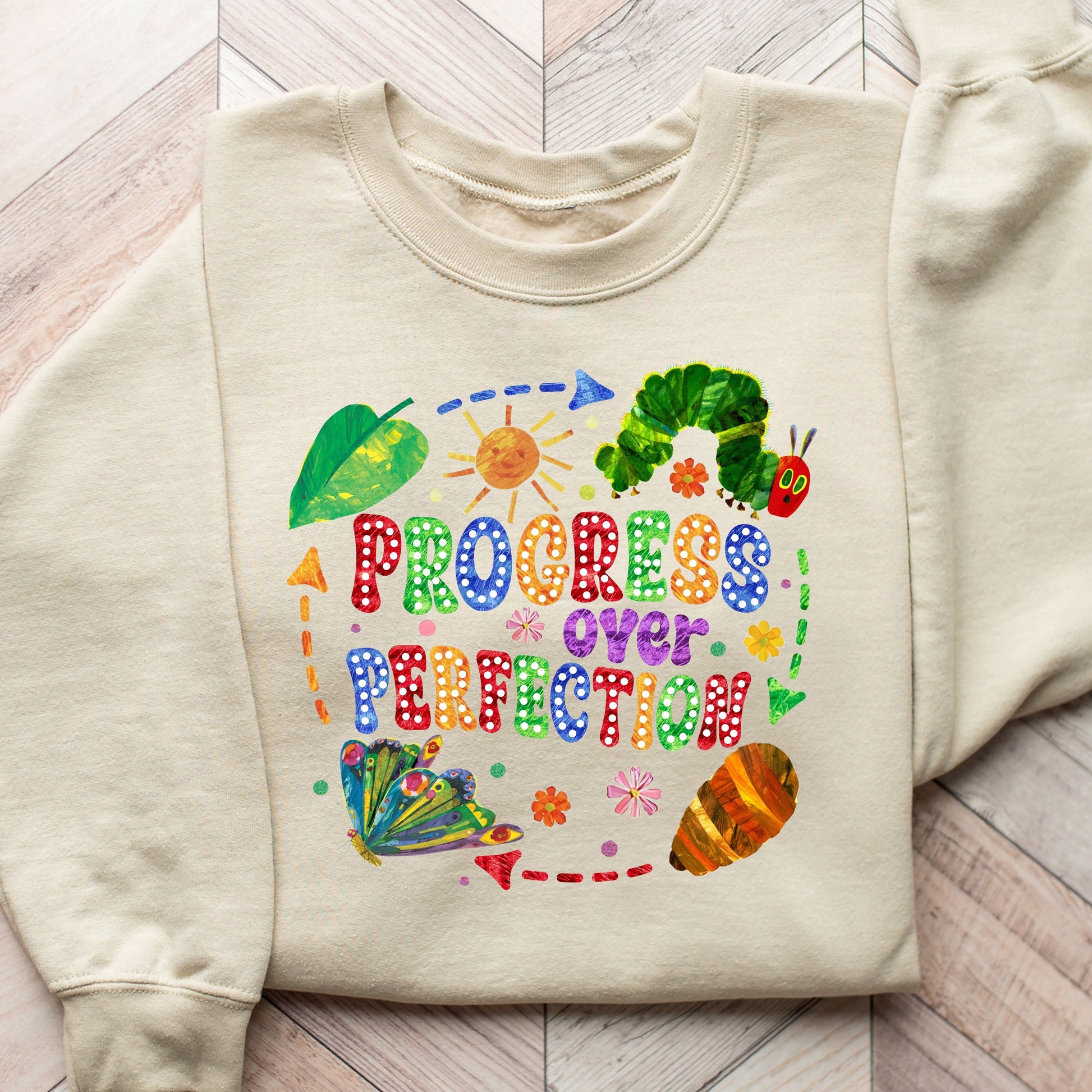 "Progress Over Perfection" DTF transfer design on a beige sweatshirt featuring a colorful caterpillar, butterfly, and uplifting typography.