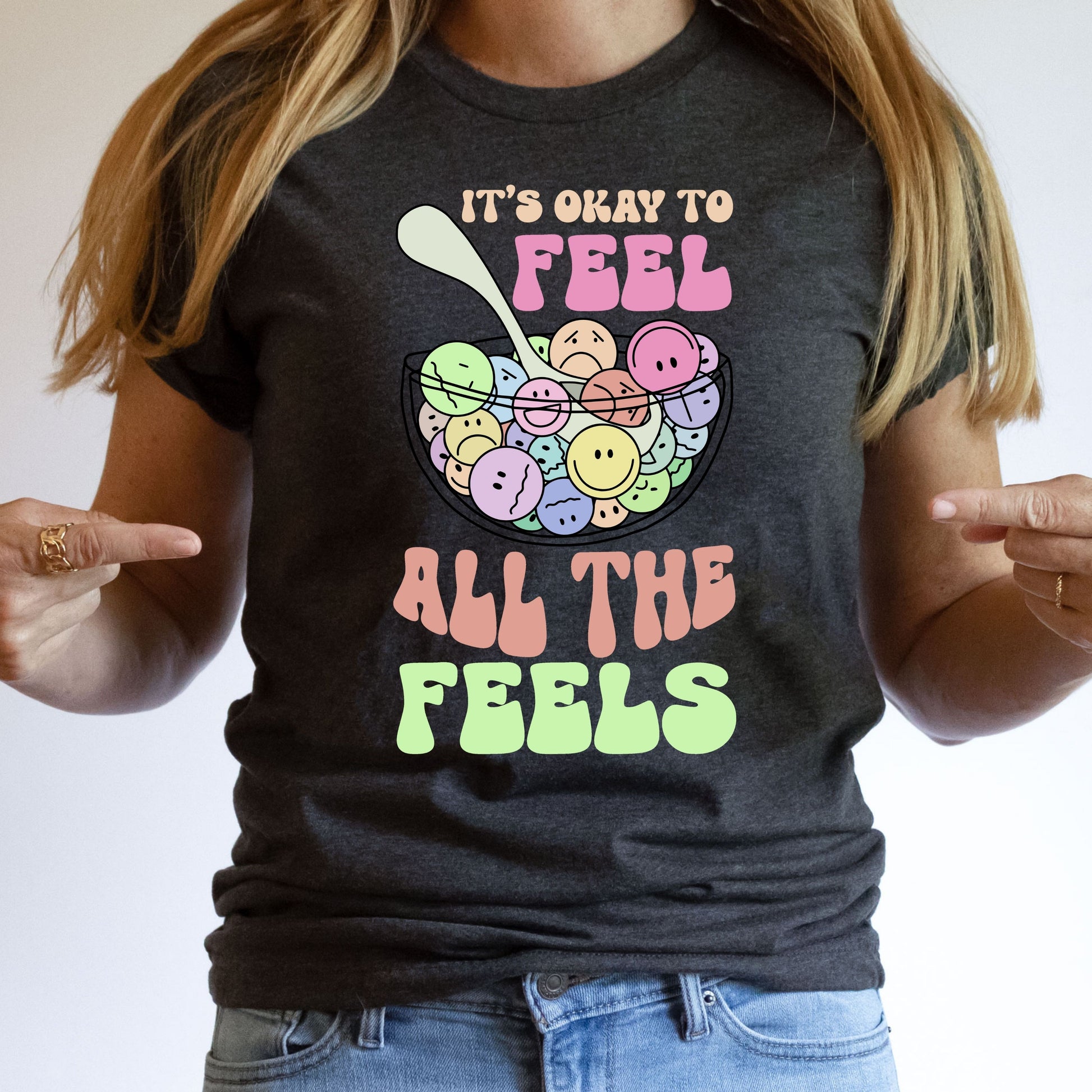 "It's Okay to Feel All the Feels" DTF transfer design on a dark gray t-shirt featuring a colorful bowl of smiley faces and uplifting typography.