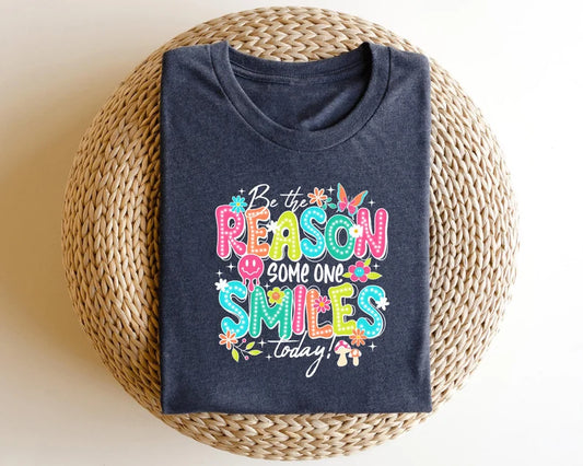 "Be the Reason Someone Smiles Today" colorful DTF transfer design on a navy t-shirt featuring cheerful typography with flowers and playful icons.