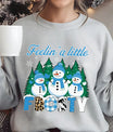 Light gray sweatshirt with “Feelin’ a Little Frosty” DTF transfer featuring three smiling snowmen, pine trees, snowflakes, and bold patterned lettering, perfect for winter apparel.