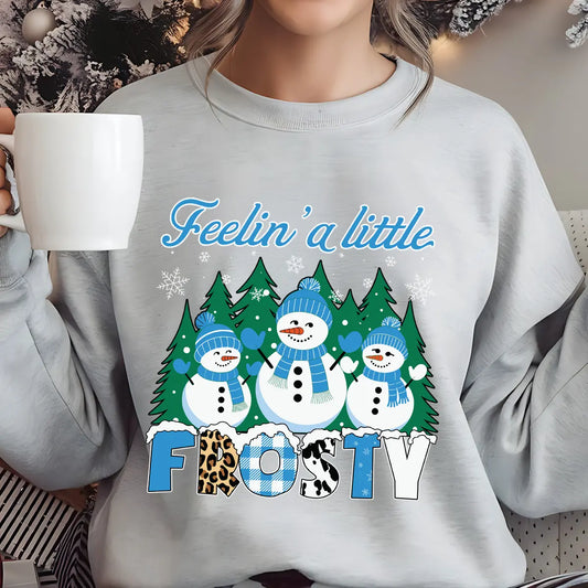 Light gray sweatshirt with “Feelin’ a Little Frosty” DTF transfer featuring three smiling snowmen, pine trees, snowflakes, and bold patterned lettering, perfect for winter apparel.