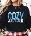 Black sweatshirt with “Cozy Season” DTF transfer featuring snow-capped blue letters, snowflakes, and cute snowmen—perfect for warm and festive winter wear.