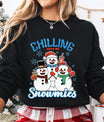 Black sweatshirt with “Chilling with My Snowmies” DTF transfer featuring three smiling snowmen in winter hats and scarves holding drinks, surrounded by snowflakes—perfect for festive apparel.