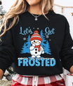 Black sweatshirt with “Let’s Get Frosted” DTF transfer featuring a smiling snowman in a red hat and scarf, blue trees, and icy text—perfect for playful winter apparel.