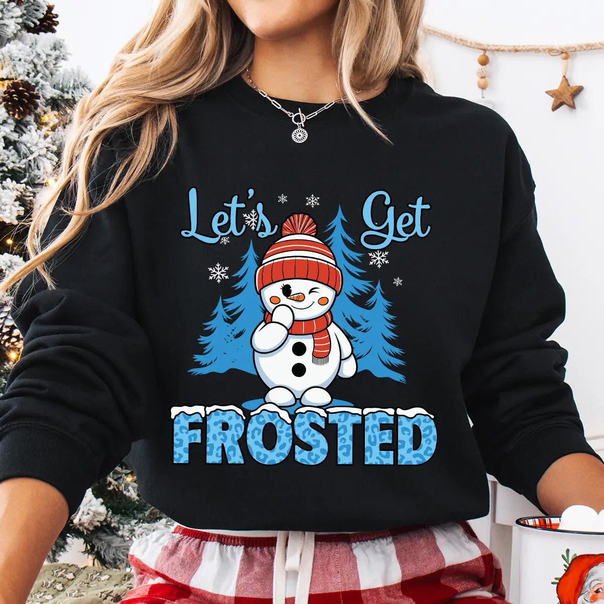 Black sweatshirt with “Let’s Get Frosted” DTF transfer featuring a smiling snowman in a red hat and scarf, blue trees, and icy text—perfect for playful winter apparel.