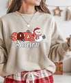 Sand-colored sweatshirt with red plaid “Cozy Season” DTF transfer featuring a smiling snowman in a Santa hat and scarf with snowflakes.