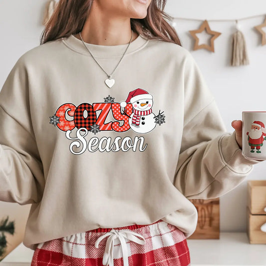 Sand-colored sweatshirt with red plaid “Cozy Season” DTF transfer featuring a smiling snowman in a Santa hat and scarf with snowflakes.