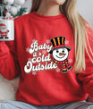 Red sweatshirt with “Baby It’s Cold Outside” DTF transfer featuring a retro snowman in an orange-and-black hat and striped scarf with snowflakes.
