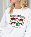 White sweatshirt with “Stay Groovy” DTF transfer featuring three smiling snowmen in red and green winter hats and scarves surrounded by stars.