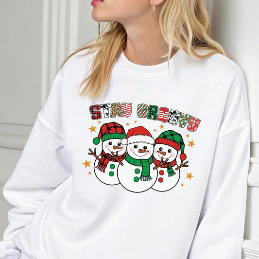 White sweatshirt with “Stay Groovy” DTF transfer featuring three smiling snowmen in red and green winter hats and scarves surrounded by stars.