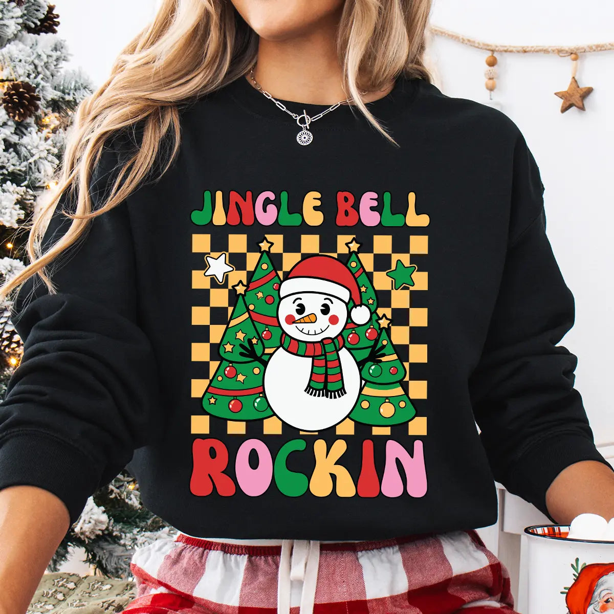 Black sweatshirt with a colorful “Jingle Bell Rockin’” design featuring a smiling snowman and Christmas trees on a yellow checkerboard background.