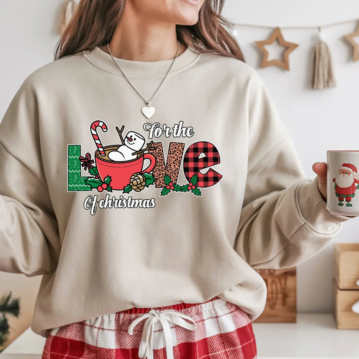 Beige sweatshirt with “For the Love of Christmas” design featuring a snowman in a red mug with candy cane, plaid letters, and festive holly decorations.