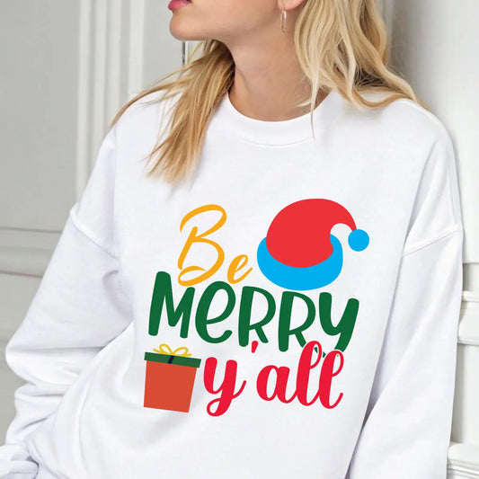 White sweatshirt with colorful “Be Merry Y’all” design featuring a Santa hat, wrapped gift, and festive lettering in red, green, yellow, and blue.