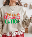 Beige sweatshirt with colorful “Christmas Cutie” text, gingerbread men garland, and small Christmas tree graphic.