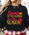Black sweatshirt with “Jesus Is the Reason for the Season” red and yellow text and cross design – faith-based Christmas sweatshirt.
