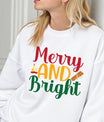 White sweatshirt with “Merry and Bright” text in red, gold, and green featuring candle and cinnamon illustrations – festive holiday apparel.