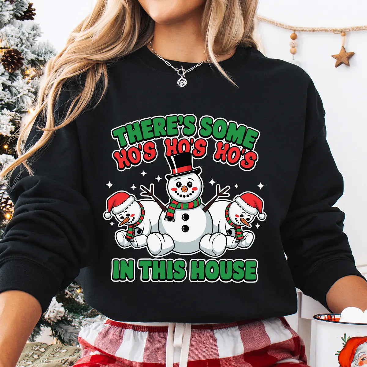 Black sweatshirt featuring three cheerful snowmen and the phrase “There’s Some Ho’s In This House” in red and green Christmas colors.
