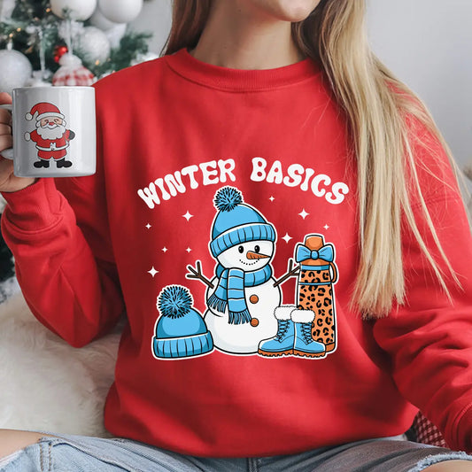 Red sweatshirt featuring a cheerful snowman in blue winter gear with a leopard-print gift and the phrase “Winter Basics” above.