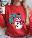 Red sweatshirt with festive snowman DTF transfer design featuring teal beanie, pink scarf, and text ’Tis the Season, ideal for Christmas or winter holiday apparel.