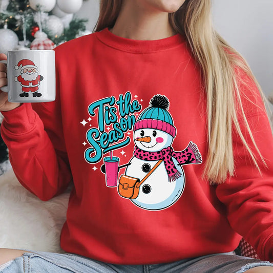 Red sweatshirt with festive snowman DTF transfer design featuring teal beanie, pink scarf, and text ’Tis the Season, ideal for Christmas or winter holiday apparel.