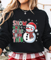 Black sweatshirt featuring a smiling snowman in a Santa hat and plaid scarf with the phrase “Snow One Cuter Than This” in festive red, green, and white lettering.